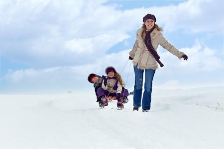 Children having fun on a sleigh in the snow with their motherの写真素材