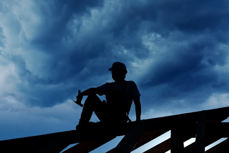 Builder resting on top of roof structure - silhouette against stormy skyの写真素材