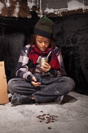 Beggar child boy reviews the money he received looking into tin canの写真素材