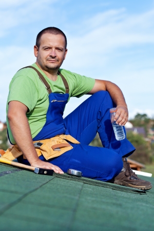 Worker laying bitumen roof shingles - resting on top of buildingの写真素材