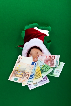 Money for the holidays - santa  handing you euro banknotes through hole in green backgroundの写真素材