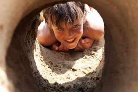 Happy boy on the beach smiling and looking through sand castle tunnelの写真素材