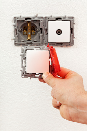 Changing a defective electrical wall fixture - male hand with a new switchの写真素材