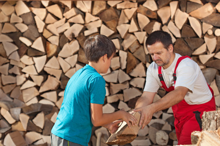 Boy helping his father stacking the firewood - handing him the piecesの写真素材
