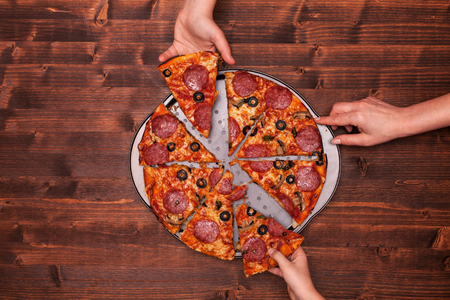 Hands taking pizza slices off the baking pan - top view, copy spaceの写真素材