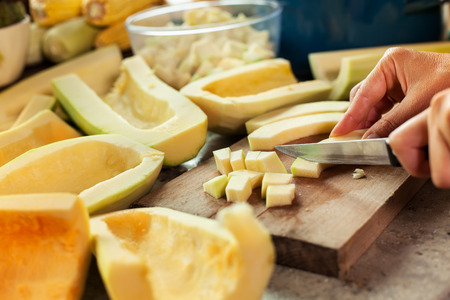 Woman chopping pumpkin slices on cutting board preparing to cook - closeupの写真素材