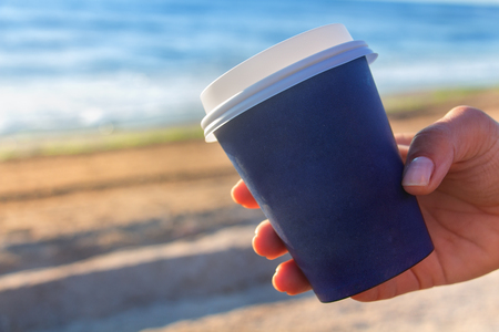 Cup of coffe to go on the sea shore - woman hand closeup, with copy spaceの写真素材