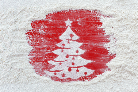 Making christmas cookies concept - flour brushed away revealing xmas tree on red tableの写真素材