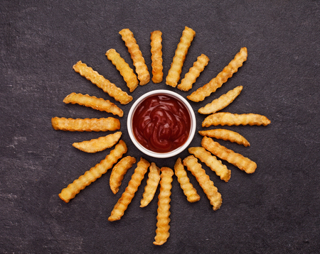 French fries and ketchup arranged in the form of flower petals on dark slate background - top viewの写真素材
