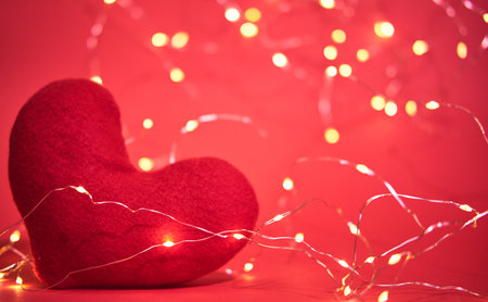 Red soft toy heart made of handmade fabric on bright red background with garland of yellow warm shade. Banner card to celebrate Valentines day or international womens day.の写真素材