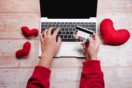 Online shopping for Valentines day on February 14. Pay for purchases and gifts online with credit card. Silver laptop with black keyboard and red toy soft hearts, freelancers desktop.の写真素材
