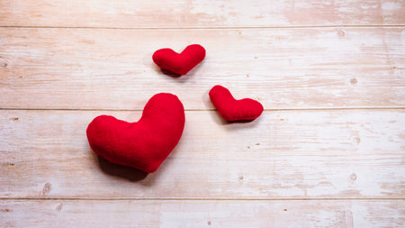 Three red toy soft plush hearts on wooden table. Flat background for Valentines day and empty space for lettering or design. Minimalistic greeting card as gift for Valentines day holiday.の写真素材