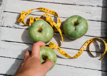 A human touches green fresh apples and a yellow centimeter ribbon with the numbers. Delicious and healthy food with vitamins for fitness and healthy lifestyle.の写真素材