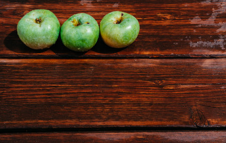 Three fresh green apples lie in a row on a wooden table. A textured mahogany wood background and fruit lie on it. Fresh autumn Apple harvest on the kitchen countertop.の写真素材