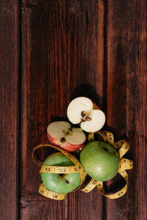 Three fresh green apples lie in a row on a wooden table and are wrapped with a yellow measuring tape. Fresh autumn Apple harvest on the kitchen countertop. Food for active people.の写真素材
