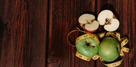 Three fresh green apples lie in a row on a wooden table and are wrapped with a yellow measuring...