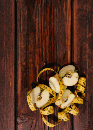 Small pieces of sliced fresh Apple lie on the mahogany kitchen table, and a yellow fitness measuring tape is next to it. A delicious and healthy snack for healthy and active people.の写真素材