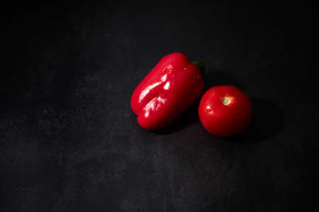 Whole wet red bell pepper and tomato on black background. Fresh vegetables on black kitchen table. Minimalistic restaurant menu.の写真素材
