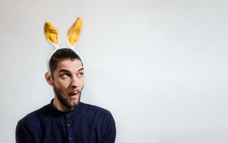 Caucasian man with yellow plush rabbit ears sits and looks away in surprise. One color creative...