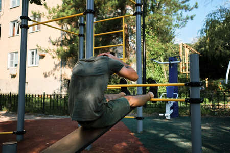 Young cute Caucasian man shakes his abs on street sports ground equipped with exercise equipment....