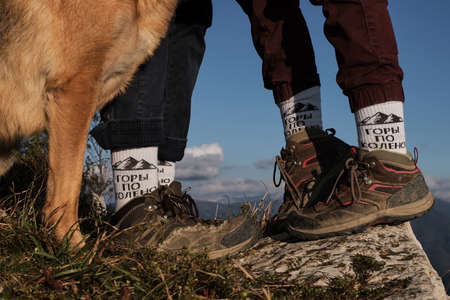 Young couple standing with shoes and a dog next to them. Inscription on socks in Russian is knee-high mountains. Motivating inscription for young people and travelers. To love freedom in mountains.の写真素材