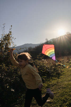 Little Caucasian cute girl runs around field at sunset and launches kite into sky. Active outdoor games. Lifestyle concept.の写真素材