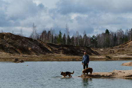 Sand Quarry. Caucasian man travels with two dogs. Human stands on small sandy island among river...