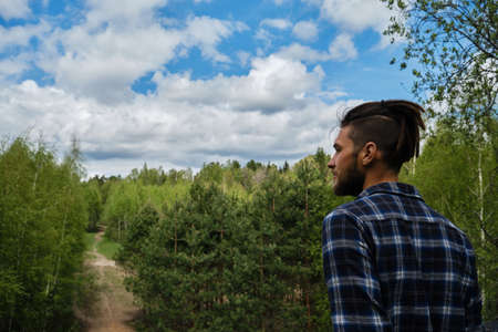 A young Caucasian man with dreadlocks and beard admires nature and forest from observation deck....