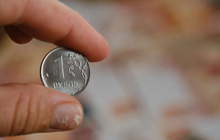 Human holds iron coin 1 ruble with hand on blurry background of five thousand paper bills. Economics and finance of Russian Federation. Sanctions and financial crisis. One cheapest coin.の写真素材