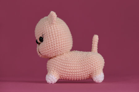 Amigurumi kitten doll on pink background. A soft DIY toy made of natural cotton and wool. Cute little crocheted cat, handmade art. side view.の写真素材