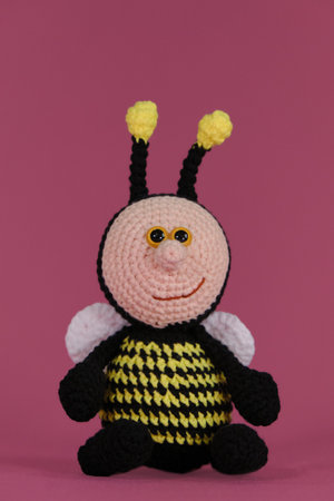 Amigurumi bumblebee doll on pink background. Soft DIY toy made of cotton. One bee black with yellow stripes and funny wings and horns crocheted, handmade art. front view.の写真素材