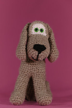 Amigurumi puppy doll sits on pink background. Soft DIY toy made of cotton. Front view, full length close up portrait. One brown dog crocheted, handmade art.の写真素材