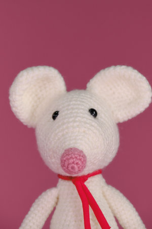 Amigurumi one white mouse with big ears and long nose on a pink background. Front view, close up portrait. A soft DIY toy made of natural cotton and wool. Cute little rat crocheted, handmade art.の写真素材
