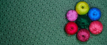Yarn for crocheting. Several woolen multicolored balls of thread on a green crocheted background. Concept hobby of handmade needlework from home. Top view, web banner with copy space.の写真素材
