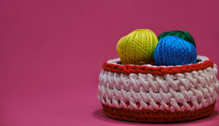 Concept craft handmade needlework hobby from home. Yarn for crocheting. Several woolen multi colored balls of thread in a wicker basket on a pink background. Side view, web banner with copy space.の写真素材