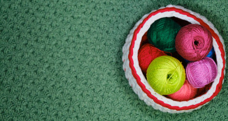 Yarn for crocheting. Top view, web banner with copy space. Concept hobby of handmade needlework from home. Several woolen multicolored balls of thread in wicker basket on a green crocheted background.の写真素材