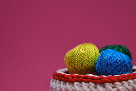 Concept craft handmade needlework hobby from home. Yarn for crocheting. Several woolen multi colored balls of thread in a wicker basket on a pink background. Side view, web banner with copy space.の写真素材