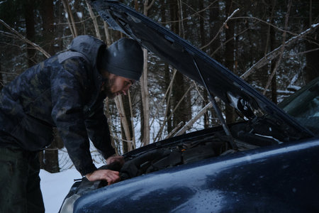 A young Caucasian man stands near the open hood of the car and checks the safety before the trip. A...