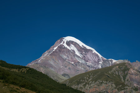 Nature of the Northern Caucasus. The snowy peak of Mount Kazbek. View from the peak in the village of Stepantsminda, Kazbegi. Blue cloudless sky. Trip to Georgiaの写真素材