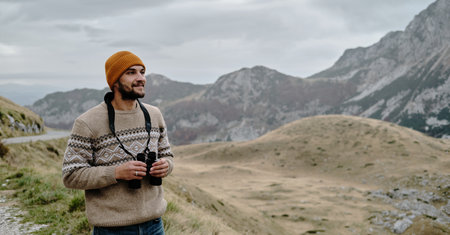 A young Caucasian man with binoculars in his hands. Montenegro country, Durmitor National Park. Saddle Pass in autumn season. Travel around the world concept. Panoramic viewの写真素材
