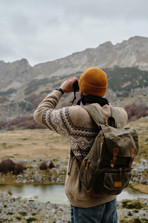 Traveler young man looking through binoculars outdoor. Montenegro country, Durmitor National Park....