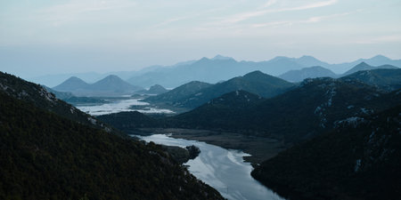 Aerial panoramic view of winding river through lush hills and mountains in Montenegro at sunset....