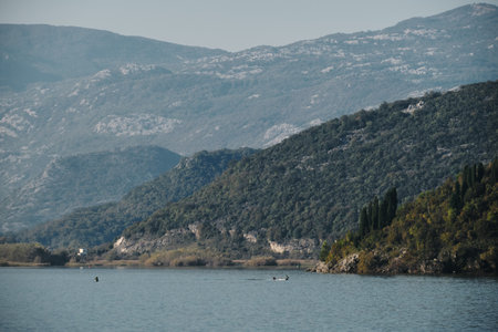 Majestic mountain slopes rise above the still waters of Skadar Lake in Montenegro, creating a serene and layered landscape bathed in morning lightの写真素材