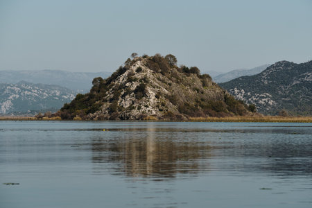 A stunning view of the lush mountains and reed-covered banks of a lake under a clear blue sky, reflecting beautifully on the still waterの写真素材