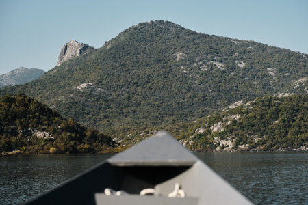 View from a boat navigating through Skadar Lake in Montenegro, approaching lush green hills and rocky mountain peaks under a clear sky. Travel conceptの写真素材
