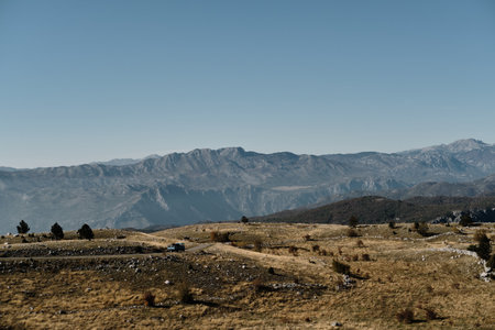 A scenic autumn landscape in the Montenegro mountains with a lone vehicle driving along a winding...