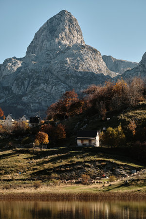 Bukumirsko Lake in the mountains of Montenegro, surrounded by colorful autumn forest and rugged peaks. Peaceful nature clear reflection in water and scenic mountain villageの写真素材
