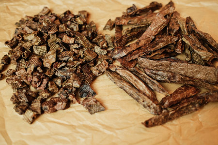Close-up of natural dried beef lung dog treats in small chunks and long strips, displayed on brown craft paper. Healthy, single-ingredient pet snacks for dogs, ideal for training or rewardingの写真素材