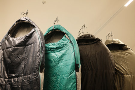 Colorful sleeping bags hanging on hooks in a gear store or rental space. Equipment for hiking, trekking, and outdoor camping, shown in a neat indoor displayの写真素材