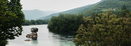 A small wooden house on a rock in the middle of the Drina River, surrounded by lush green hills in Serbia country in spring season.の写真素材